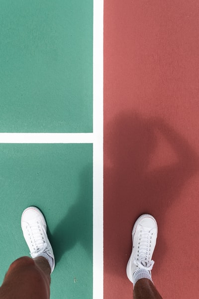 People wearing white sneakers stood between the pavement of green and red
